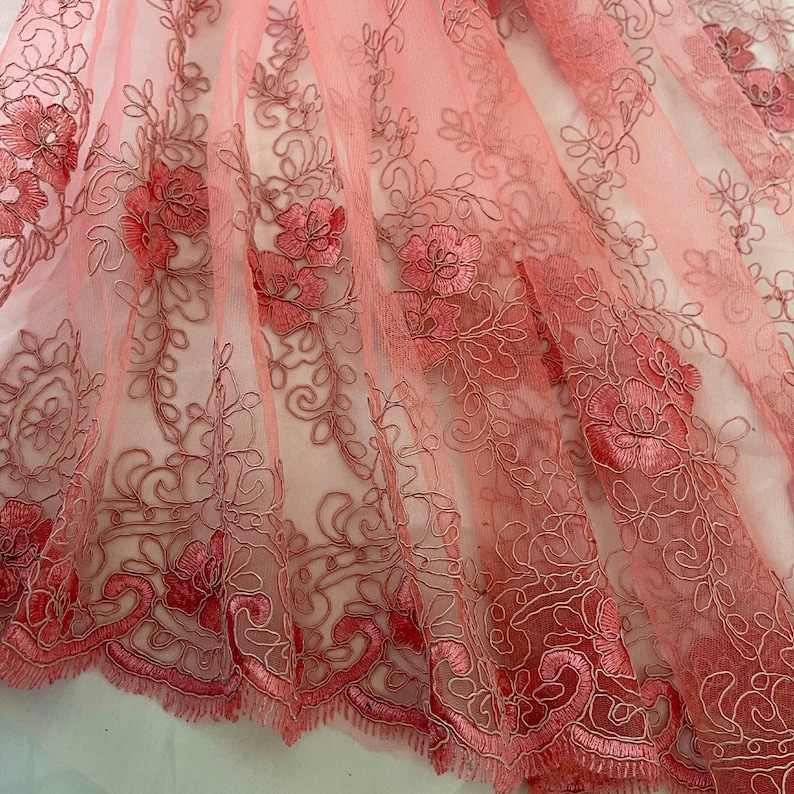 May include: Pink sheer fabric with delicate floral embroidery. The embroidery is in a darker shade of pink and creates a delicate and feminine design.