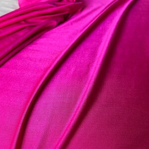 May include: Close-up of a vibrant pink fabric with a smooth, silky texture. The fabric is folded and draped, creating soft, flowing lines.