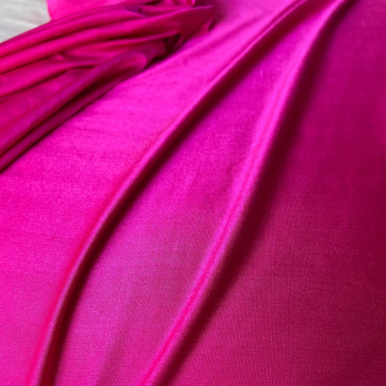 May include: Close-up of a vibrant pink fabric with a smooth, silky texture. The fabric is folded and draped, creating soft, flowing lines.