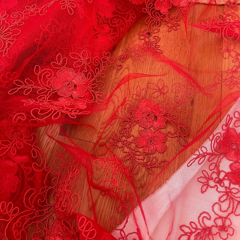 May include: Red lace fabric with a floral pattern. The lace is delicate and intricate, with small flowers and leaves.