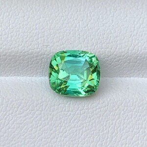 May include: A cushion-cut green gemstone with a slight blue hue.