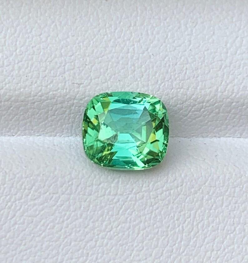 May include: A cushion-cut green gemstone with a slight blue hue.