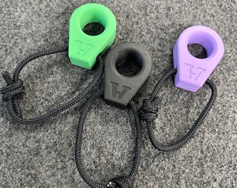 May include: Three colorful ring-shaped accessories with black cords. One is green, one is black, and one is purple. Each has a raised letter "V" on the front. The cords are knotted at the end.