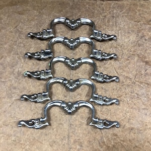 May include: Five silver drawer pulls with ornate designs. The pulls are in a row, with the top pull slightly offset from the others.