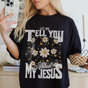 「Let Me Tell You About My Jesus」シャツ、女性用クリスチャングラフィックTシャツ、デイジーがあしらわれた信仰Tシャツ、大胆な聖書の一節シャツ、礼拝シャツギフト