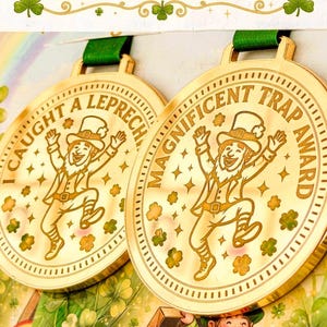 May include: Two gold medals with green ribbons. Each medal features a cartoon leprechaun and the text "I Caught a Leprechaun" and "Magnificent Trap Award". The image includes the text "Two Medals to Choose From".