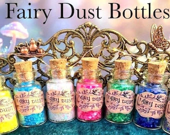 May include: A collection of seven small glass bottles filled with colorful glitter, labeled "Fairy Dust." The bottles are corked and displayed on a decorative, ornate tray. The text "Fairy Dust Bottles" is at the top of the image.
