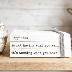 May include: A decorative white artichoke sculpture and a stack of three white books with the words "Happiness is not having what you want it's wanting what you have" printed on them. The books are tied with a gray string.