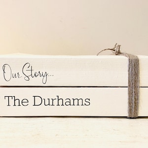 Peut inclure: Deux blocs de bois blancs empilés l'un sur l'autre. Le bloc supérieur porte le texte "Our Story..." et le bloc inférieur porte le texte "The Durhams". Les blocs sont liés ensemble par un morceau de ficelle.
