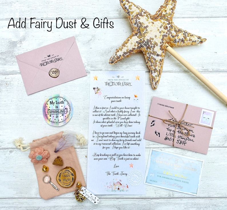 Peut inclure: Ensemble de cadeaux et de papeterie sur le th&egrave;me des f&eacute;es. Comprend une baguette &eacute;toile dor&eacute;e, une enveloppe rose, une lettre, une pochette avec des bibelots et un autocollant "My Tooth is Sparkling". Le texte "Add Fairy Dust & Gifts" est en haut.