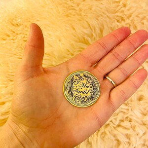 Puede incluir: Una moneda navide&ntilde;a dorada con el texto "I Met Santa" en una fuente decorativa. La moneda presenta un dise&ntilde;o de corona con una ilustraci&oacute;n de trineo y Pap&aacute; Noel. La moneda se sostiene en una mano.