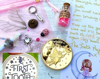 May include: A collection of fairy-themed items, including a gold coin with a fairy design, a small glass bottle with pink contents, a key charm, a ladybug figurine, and a "First Tooth" keepsake. The items are arranged with a handwritten note and fairy wings.