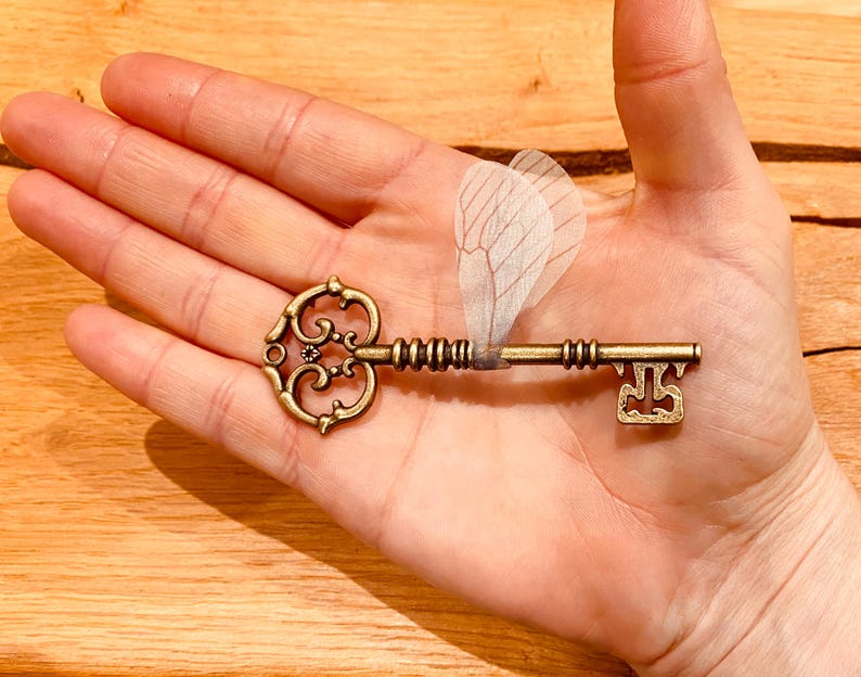 May include: A gold-toned skeleton key with a decorative heart-shaped head and a delicate, translucent butterfly wing attached to the shaft.