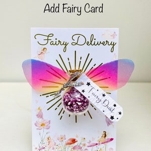 May include: A whimsical card with the words "Fairy Delivery" and "Fairy Dust." The card features a small glass bottle filled with pink glitter, adorned with iridescent wings. The words "Add Fairy Card" are at the top.