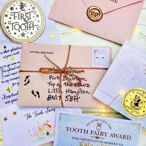 Peut inclure: Ensemble d'articles sur le th&egrave;me de la F&eacute;e des dents, comprenant un souvenir dor&eacute; "Premi&egrave;re dent", des enveloppes roses, un certificat et une enveloppe de livraison sp&eacute;ciale avec une adresse manuscrite. Les articles sont dispos&eacute;s sur une surface blanche avec des guirlandes lumineuses et des &eacute;toiles.