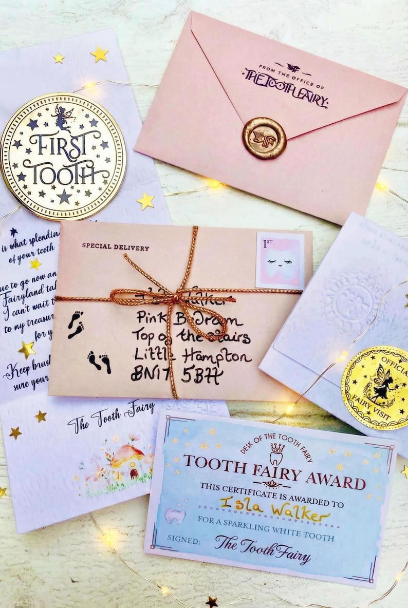 Peut inclure: Ensemble d'articles sur le th&egrave;me de la F&eacute;e des dents, comprenant un souvenir dor&eacute; "Premi&egrave;re dent", des enveloppes roses, un certificat et une enveloppe de livraison sp&eacute;ciale avec une adresse manuscrite. Les articles sont dispos&eacute;s sur une surface blanche avec des guirlandes lumineuses et des &eacute;toiles.