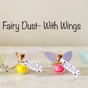 May include: Four small glass bottles filled with colorful glitter, each with a cork stopper and a tag that reads "Fairy Dust". Each bottle has a pair of attached wings. The text "Fairy Dust - With Wings" is above the bottles.