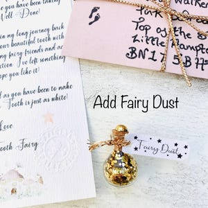 Peut inclure: Une petite bouteille en verre remplie de paillettes dor&eacute;es, &eacute;tiquet&eacute;e "Fairy Dust", est pos&eacute;e &agrave; c&ocirc;t&eacute; d'une note de la F&eacute;e des dents. La bouteille a un bouchon en li&egrave;ge et est attach&eacute;e avec de la ficelle. Une enveloppe rose avec une ficelle dor&eacute;e est &eacute;galement dans l'image.