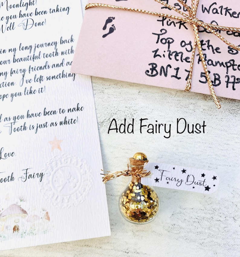 Peut inclure: Une petite bouteille en verre remplie de paillettes dor&eacute;es, &eacute;tiquet&eacute;e "Fairy Dust", est pos&eacute;e &agrave; c&ocirc;t&eacute; d'une note de la F&eacute;e des dents. La bouteille a un bouchon en li&egrave;ge et est attach&eacute;e avec de la ficelle. Une enveloppe rose avec une ficelle dor&eacute;e est &eacute;galement dans l'image.