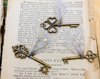 May include: Three antique brass-colored metal keys with intricate bow designs, each featuring translucent, iridescent insect-like wings attached to the shaft. The wings on the keys are decorated with small gold glitter flakes and a delicate vein pattern.