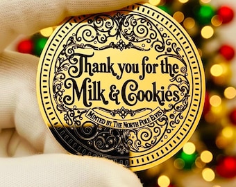 May include: A circular gold-colored coin featuring black engraved text that reads Thank you for the Milk & Cookies and Minted by The North Pole Elves. The coin has an ornate decorative border with intricate scrollwork and a dotted outer edge.