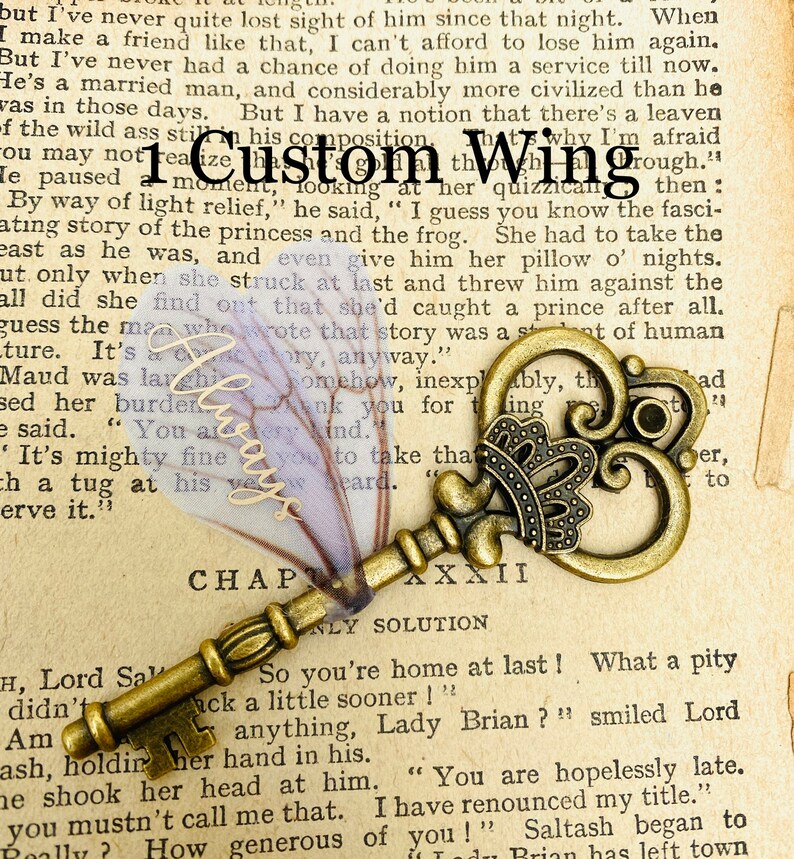 May include: A vintage-style, ornate, gold-toned skeleton key with a decorative crown on the bow. The key is lying on a page of a book with the text "Chapter XXXII" and "Only Solution" visible. The book page is yellowed and has a faded, purple, floral pattern.