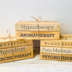 May include: Three stacks of books tied with twine. The books have aged, beige covers with black text. The titles include "Hypnotherapy," "Aromatherapy," "Nutrition," "Physiology," "Exercise Therapy," "Human Anatomy," "Pain Management," and "Psychotherapy."