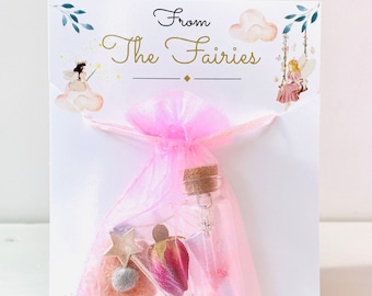 May include: A pink tulle bag with a small glass bottle inside. The bag is tied with a pink ribbon and has a card attached to it that says "From The Fairies".