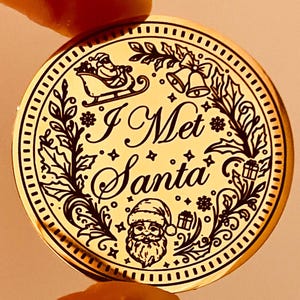 Puede incluir: Un adorno navide&ntilde;o redondo de color dorado con el texto "I Met Santa". El adorno presenta un dise&ntilde;o detallado de Pap&aacute; Noel en su trineo, campanas, regalos y follaje festivo. El dise&ntilde;o es en negro.