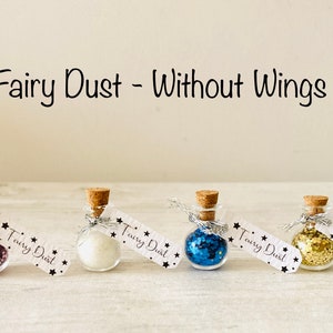 May include: Four small glass bottles with cork stoppers, each filled with a different color of glitter. The bottles are labeled "Fairy Dust" and are tied with silver ribbon. The text "Fairy Dust - Without Wings" is above the bottles.