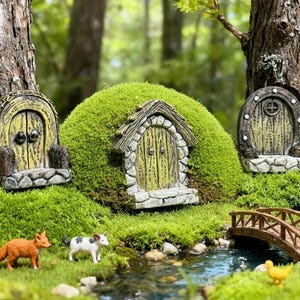 May include: A miniature fairy garden scene with three fairy doors set in green moss. A small bridge spans a stream, and miniature figurines of a fox, cow, and ducks enhance the magical forest setting.