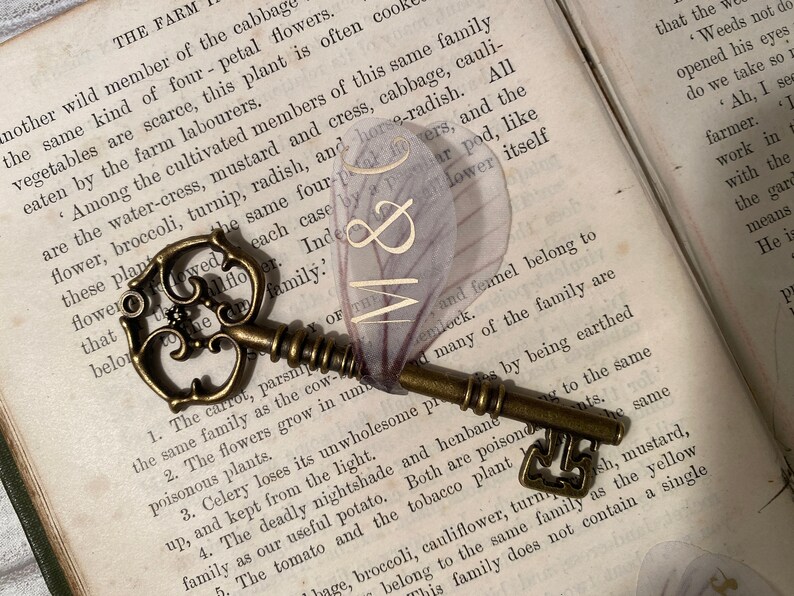 May include: A vintage skeleton key with a decorative floral design, resting on an open book with text about different types of plants and flowers. The key is made of brass and has a worn, antique finish. The book is open to a page with the text "THE FARM" at the top.