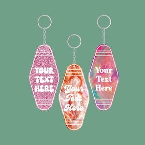 May include: Three motel-style keychains with silver key rings and chains. The keychains are in pink glitter, orange and white marbled, and a colorful swirl design. Each keychain has the text "YOUR TEXT HERE" in white.