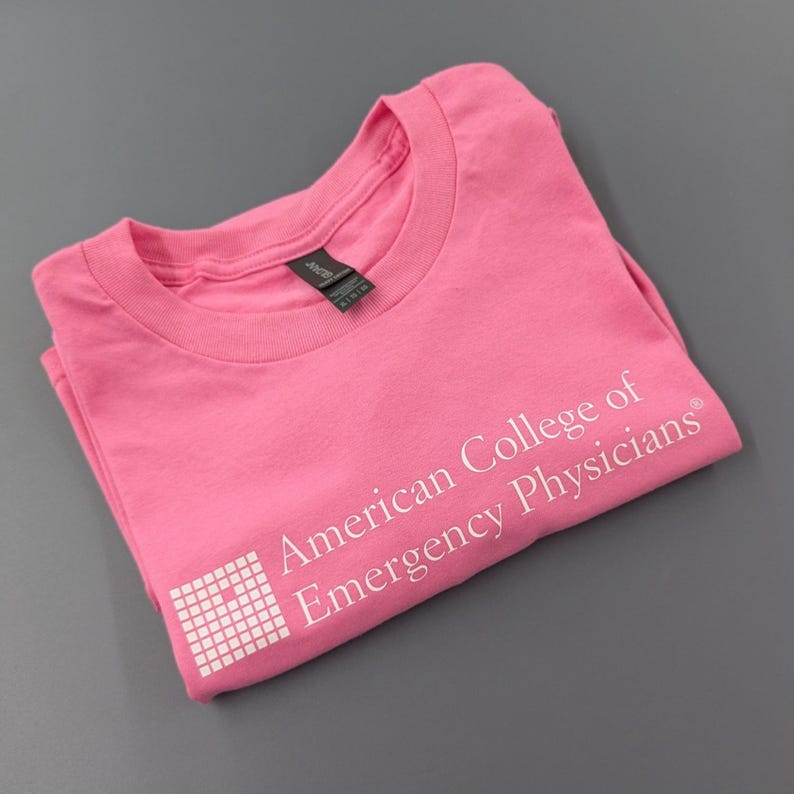 May include: A folded pink t-shirt with the text "American College of Emergency Physicians" printed in white. The shirt has a crew neck and short sleeves. The shirt is made of a soft material.