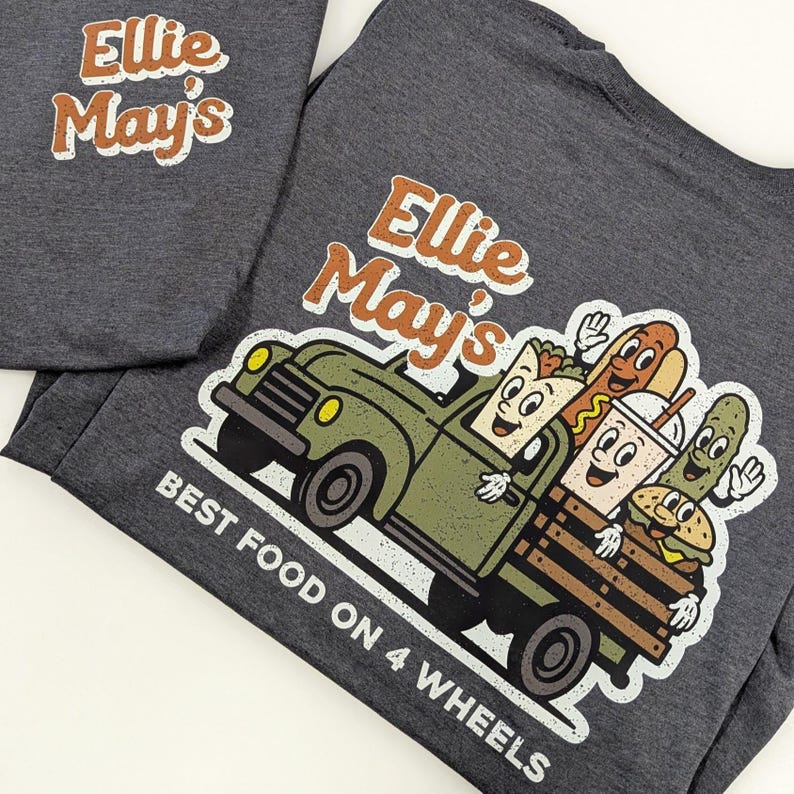 May include: Two dark grey t-shirts. One displays the text "Ellie May's" in orange and white. The other features a cartoon truck loaded with food, including a hot dog and burger, with the text "Best Food on 4 Wheels".