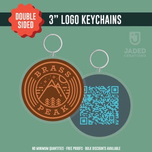 May include: Double-sided 7.6 cm logo keychains. One side features a brown circular design with the text "Brass Peak" and a mountain and tree graphic. The other side has a QR code. The keychains have a silver keyring.