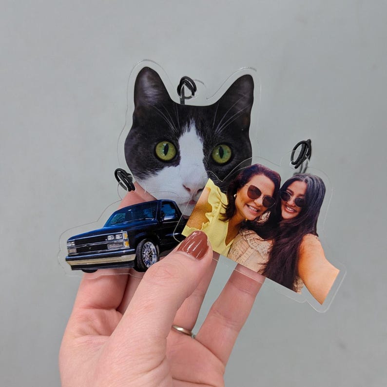 Puede incluir: Adornos fotogr&aacute;ficos personalizados de acr&iacute;lico transparente. Los adornos presentan una camioneta negra, una cara de gato en blanco y negro y una foto de dos mujeres. Cada adorno tiene un peque&ntilde;o lazo para colgar.
