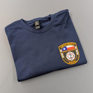 May include: Navy blue t-shirt with a patch featuring the text "Smith County Emergency Services District ESD 2 Winona Fire-Rescue". The patch includes a Texas flag and the year 2007.