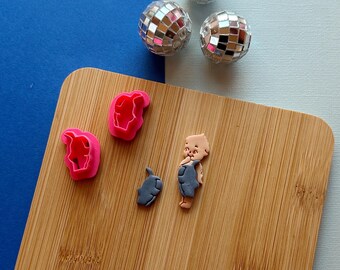 May include: A wooden cutting board with three pink cookie cutters, a gray cookie cutter, and a small figurine. Three disco balls are in the background. The background is blue and light blue.