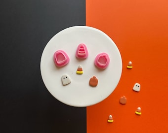 May include: A white plate with pink and white Halloween-themed clay shapes, including ghosts, pumpkins, and candy corn. The plate is on a black and orange background.