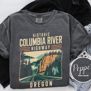 A gray t-shirt with a graphic design depicting the Historic Columbia River Highway in Oregon, along with a denim jacket and a pair of jeans.