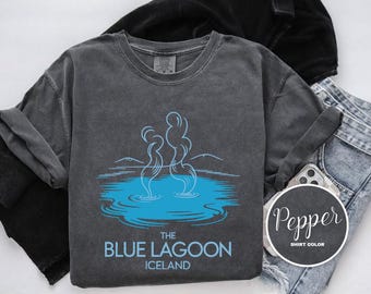 May include: A charcoal gray long-sleeve shirt with a blue graphic of the Blue Lagoon in Iceland. The graphic shows steam rising from the water. The text "THE BLUE LAGOON ICELAND" is below the graphic.
