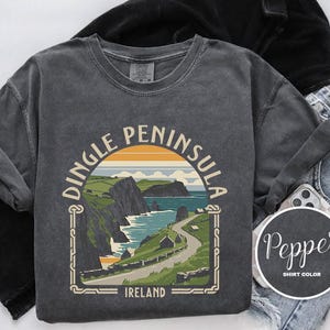 May include: A dark gray t-shirt with a vintage-style graphic of the Dingle Peninsula in Ireland. The graphic features a scenic coastal view with a winding road and the text "Dingle Peninsula, Ireland".