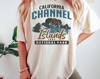 Op de afbeelding: Een crèmekleurig T-shirt met een vintage-stijl grafisch ontwerp met de tekst "California Channel Islands National Park" en een afbeelding van eilanden en water. De tekst "1980" is ook in het ontwerp opgenomen.