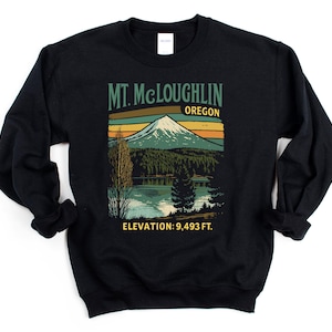 Op de afbeelding: Zwarte sweatshirt met een afbeelding van Mt. McLoughlin, Oregon. Het ontwerp toont een berg, een meer en bomen, met de tekst "Mt. McLoughlin Oregon" en "Elevation: 9,493 ft.", wat ongeveer 2893 meter is.