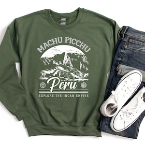 Puede incluir: Una sudadera verde con un diseño gráfico blanco de Machu Picchu, Perú. El texto "Explore the Incan Empire" está impreso debajo del gráfico.
