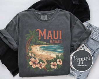 May include: A dark grey t-shirt with a vintage-style graphic of a beach scene with palm trees and the text "Maui Hawaii".