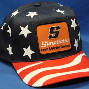 May include: A blue and red baseball cap with a white star pattern. The cap has a patch with the text "Simplicity Lawn & Garden Tractors" and a large "S" in orange.
