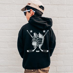 Puede incluir: Sudadera con capucha negra con un dise&ntilde;o de hockey blanco en la espalda. El dise&ntilde;o incluye un pat&iacute;n de hockey, casco, palos cruzados, un disco y el nombre "MASON". Dos estrellas est&aacute;n encima de los palos.