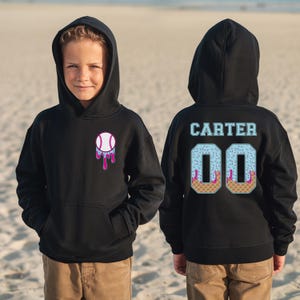 May include: Black hooded sweatshirt featuring a baseball graphic with a melting ice cream design on the front. The back displays the name "Carter" and the number "00". The sweatshirt is worn by a child.